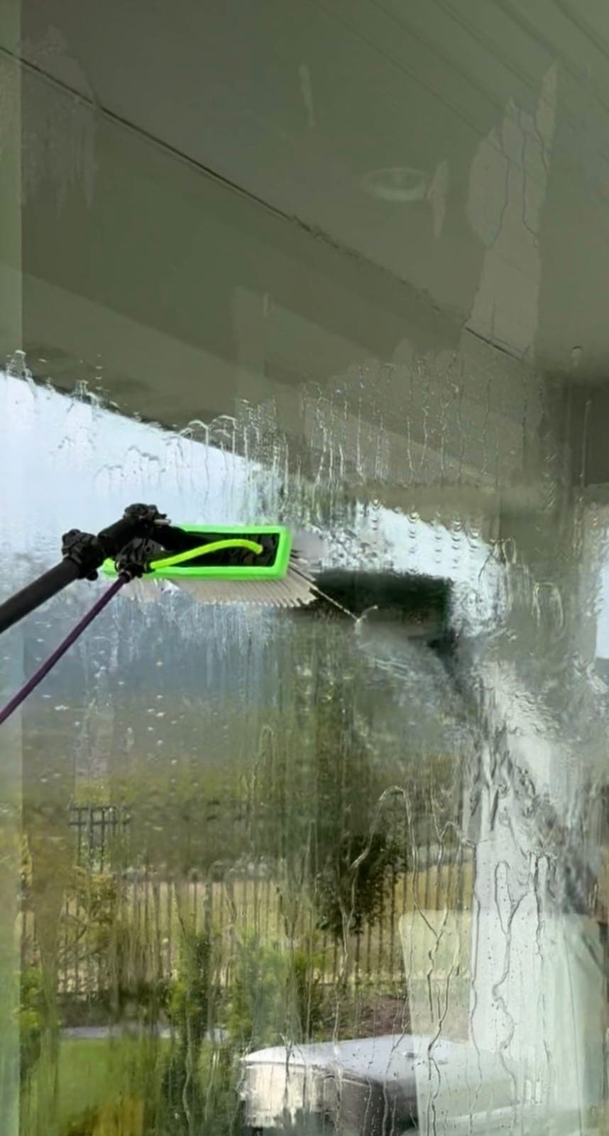 Water-fed pole brush rinsing an upper window with purified water mid-clean